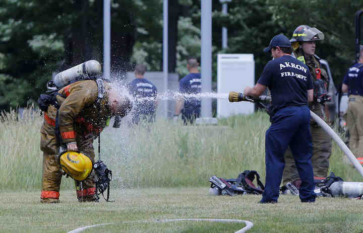 Firefighters from the Akron Fire Department are hosed down as a precaution after being in contact with a chemical at the scene of a fire in one of the buildings at the Bridgestone Americas Technical Center in Akron. None of the firefighters were injured.   (Karen Schiely / Akron Beacon Journal)